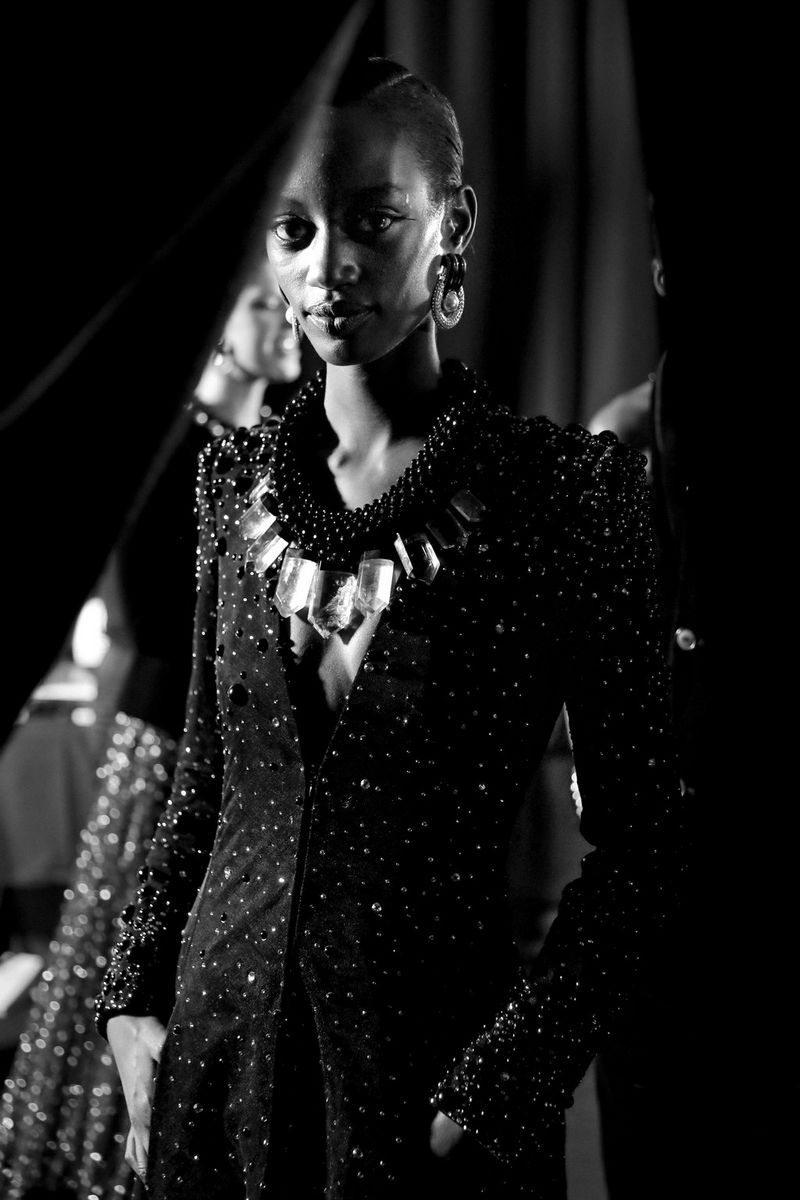 A black-and-white shot of a model peering around a curtain.