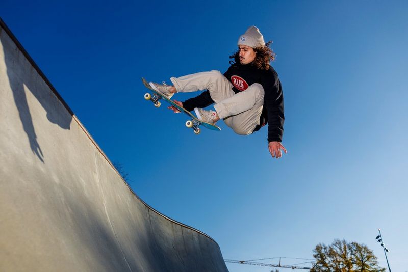 Een skateboarder met lang krullend haar die van een helling af springt, met achter hem blauwe lucht.