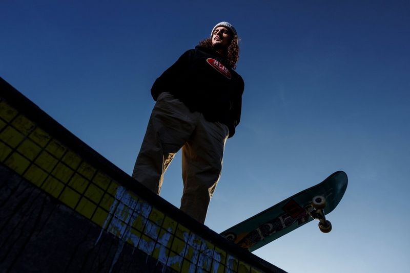 Een skateboarder op het hoogste punt van een drop, van onderaf gefotografeerd terwijl zijn board boven de rand uitsteekt.