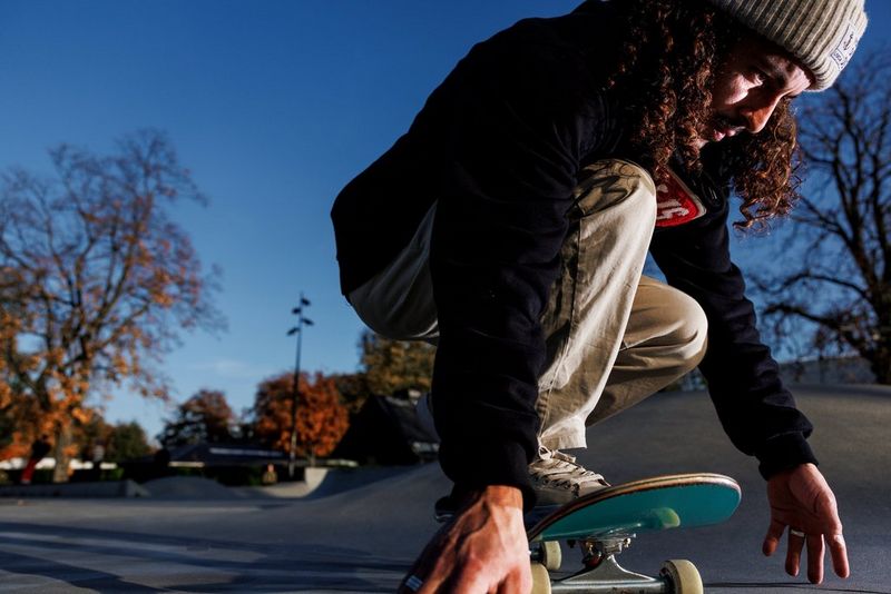 Een skateboarder zit gehurkt op zijn board, van dichtbij gefotografeerd.