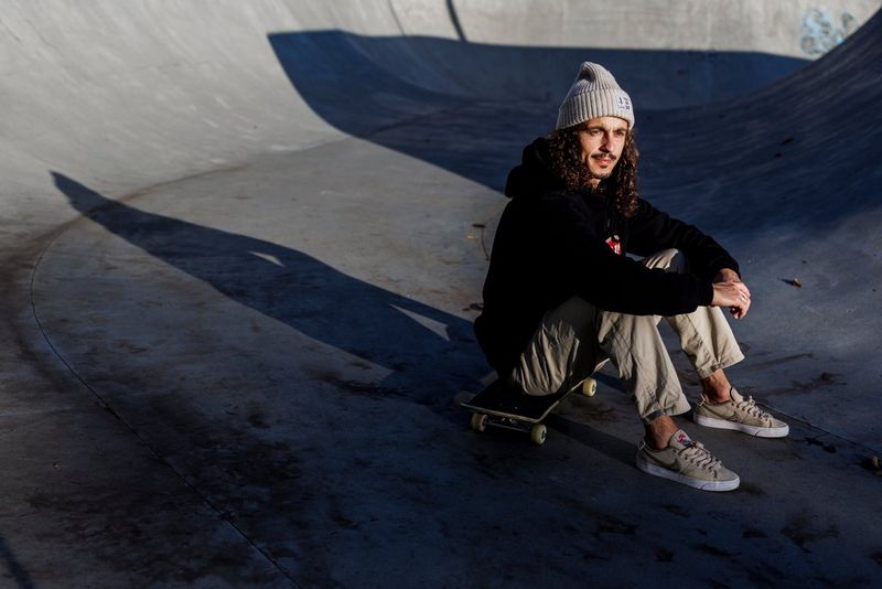 Een skateboarder zit op zijn skateboard in een skatepark-bowl, met zijn armen om zijn knieën.