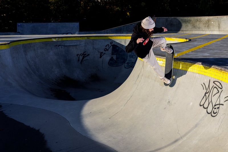 Een skateboarder boven aan een bowl met gele tegels langs de rand, in een skatepark.