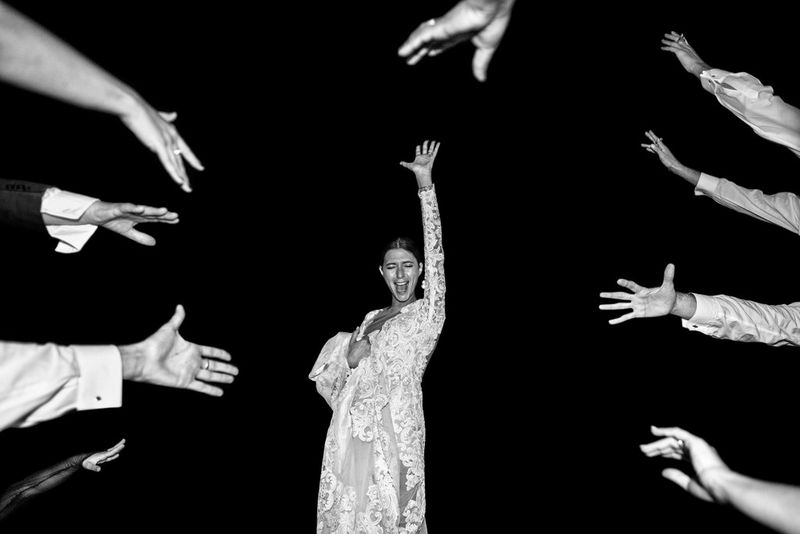 Черно-белое изображение женщины в платье, которая словно изолирована на фоне кромешной темноты; в кадр при этом тянутся девять рук.