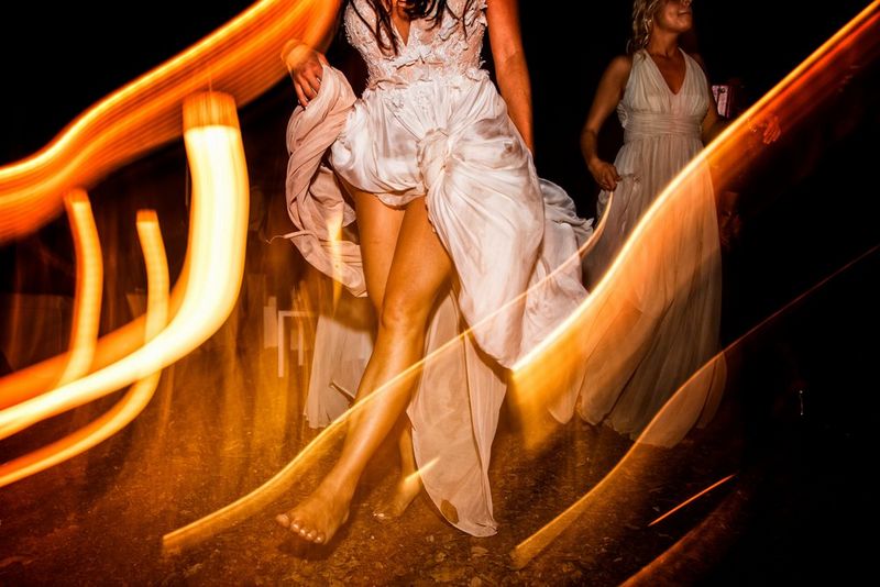 Женщина в белом платье идет босиком по улице ночью. Длительная выдержка помогла запечатлеть оранжевые световые полосы.