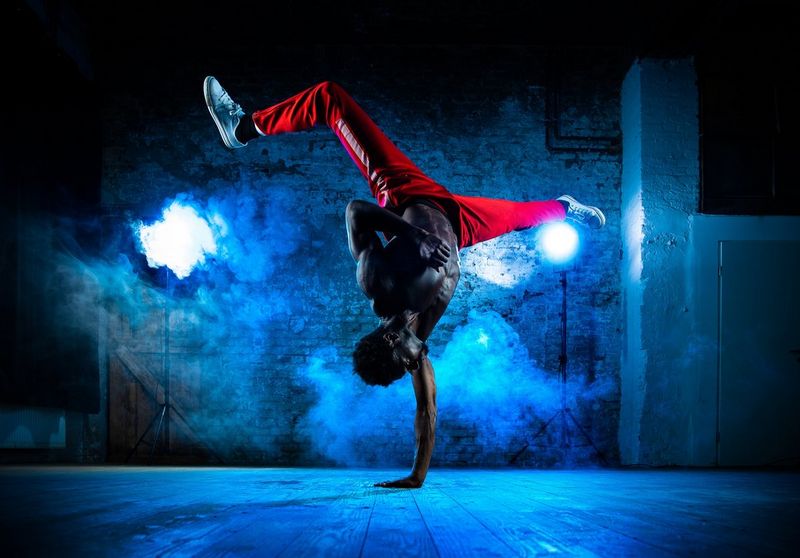 A breakdancer captured performing a one-armed handstand, his legs wide apart in the air above him.