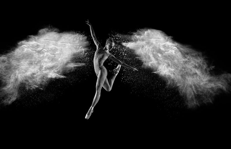 A black and white image of a ballet dancer leaping in the air, arms outstretched, with clouds of flour forming the shape of wings to both sides.