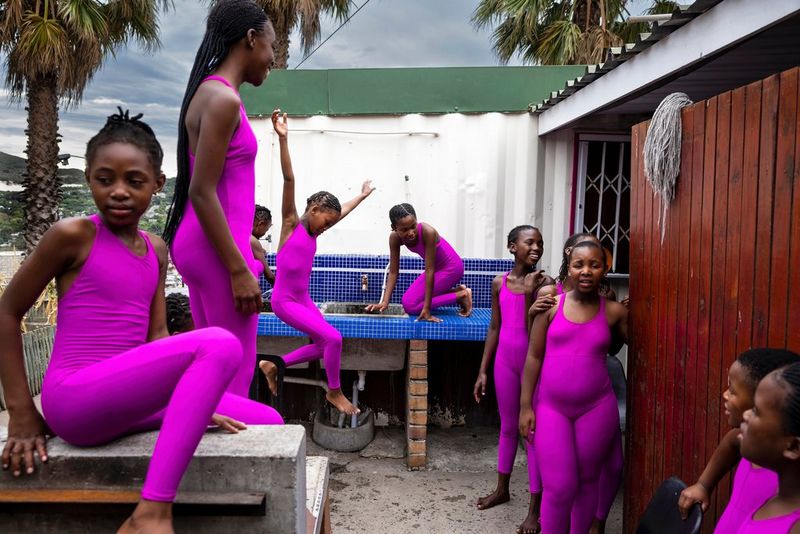 Un gruppo di ragazze in body e leggings rosa identici socializzano fuori da un piccolo edificio. Scatto realizzato da Brent Stirton con Canon EOS R5.