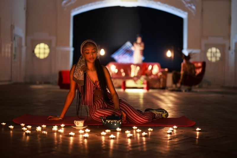 A young woman in a headscarf lounging on a roll mat, surrounded by small candles on the floor.