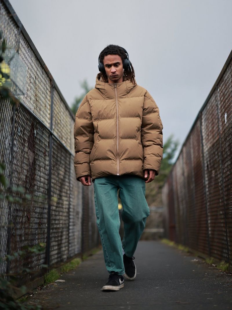A man wearing headphones and a beige jacket walking along a path.