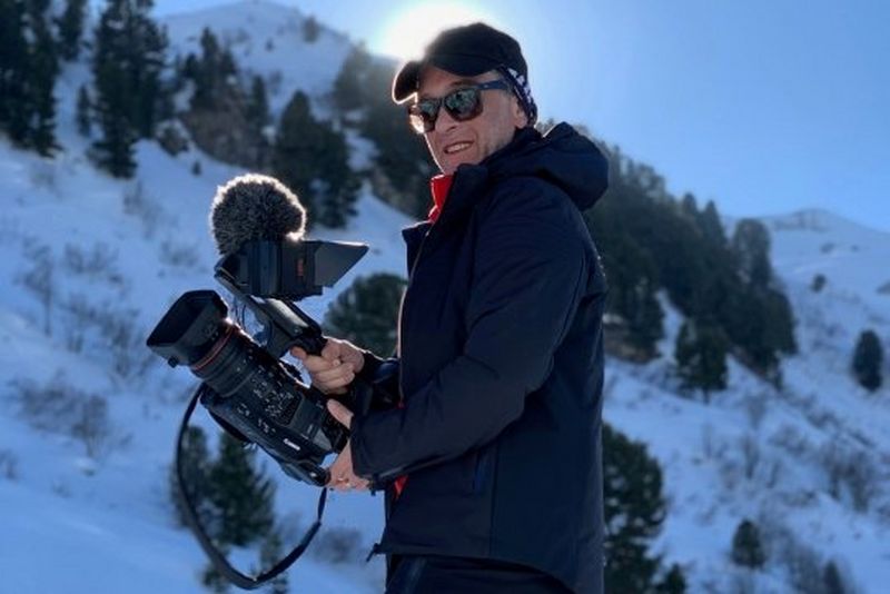 A man in winter clothing on a snowy mountainside with a Canon XF705 camcorder.