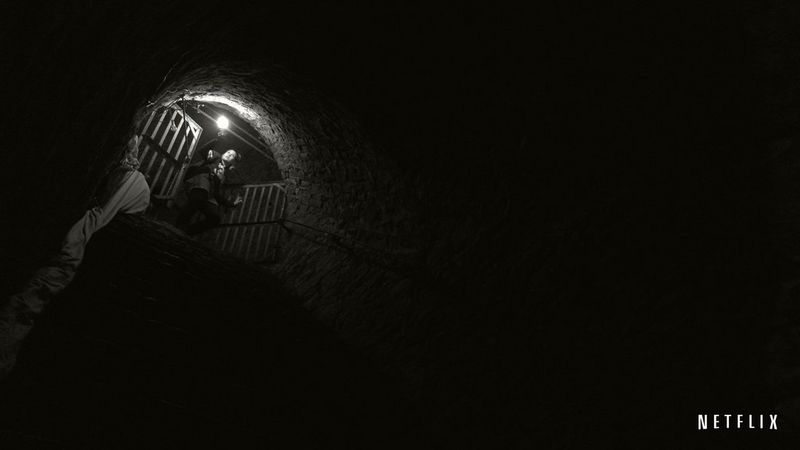 Женщина стоит на верхней ступеньке каменной лестницы, которую освещает только фонарь в ее руке.