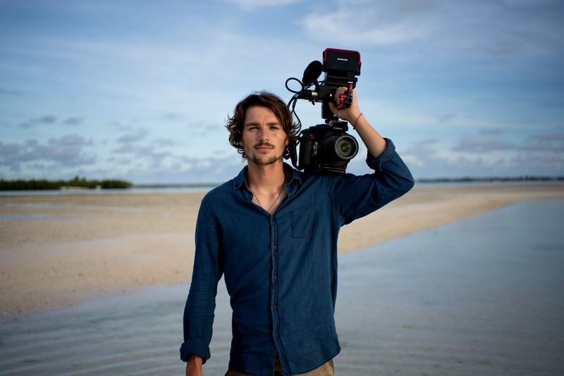 Filmmaker Jack Harries stands on a beach holding a Canon EOS C300 Mark II camera on his shoulder.