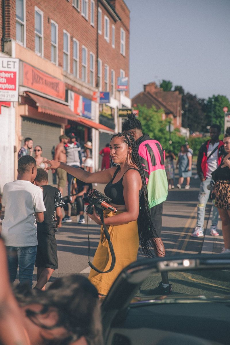 Filmmaker Ashleigh Jadee stands on a busy city street on a sunny day, directing people around her.