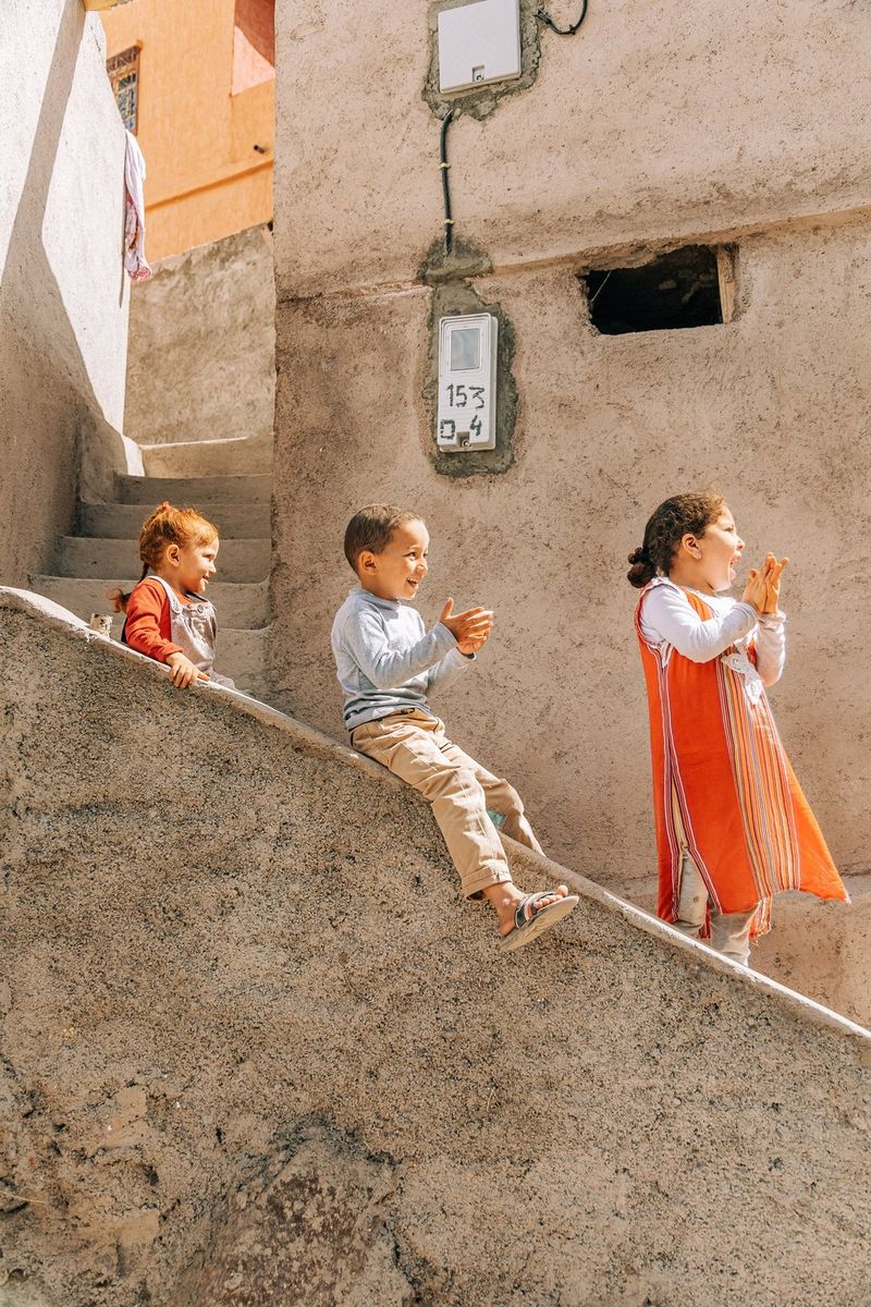 Three young children clapping, playing on a set of steep stone steps in Morocco. 