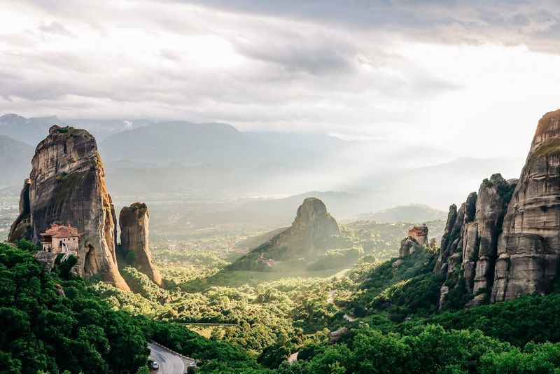 A late afternoon scene with buildings clinging to large, steep rock formations in the striking, verdant valley of Meteora, Greece. 