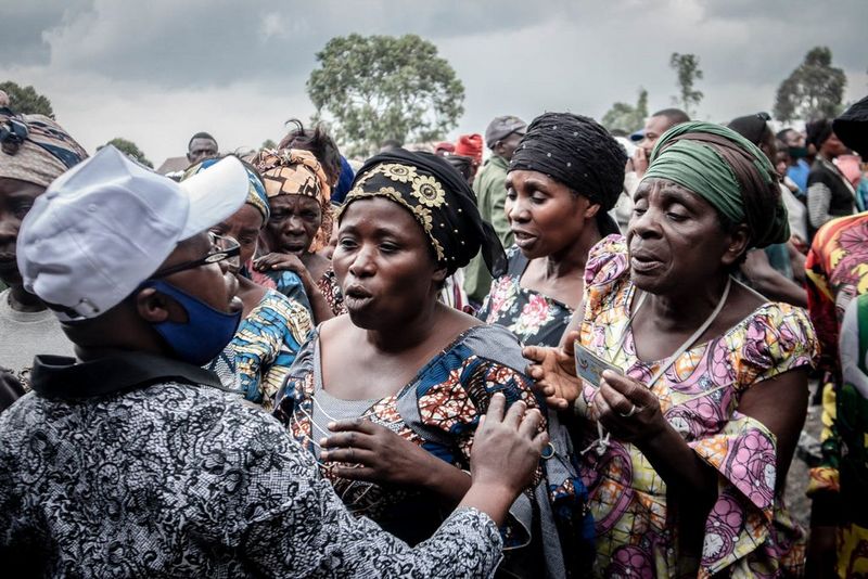 A group of women in colourful, traditional Congolese clothing and headscarves talking to a man with a baseball cap.