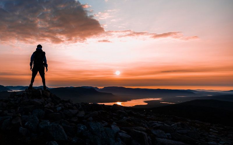 Questo scatto di Harrison Brown ritrae la silhouette di una persona che si erge su una collina dinanzi all'alba rosata.