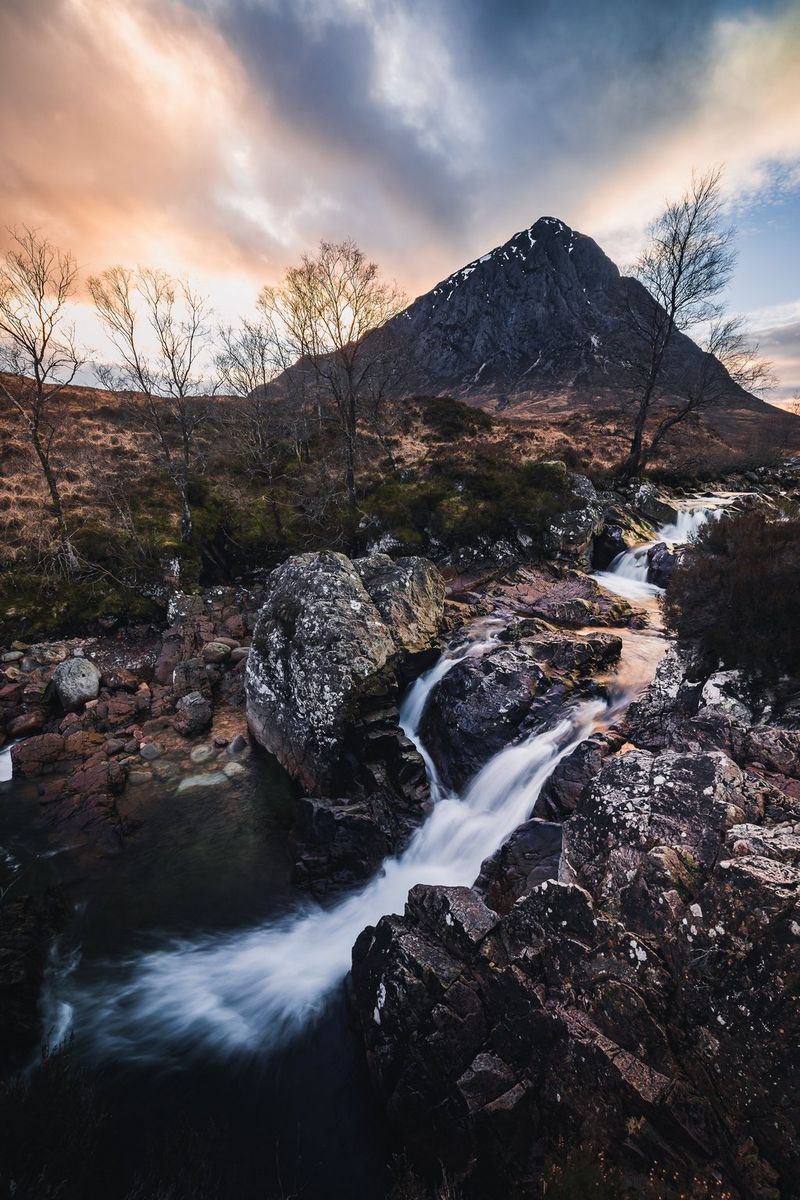 Un'esposizione lunga di Harrison Brown che ritrae un ruscello che scorre tra le rocce e gli alberi spogli, con le montagne sullo sfondo.