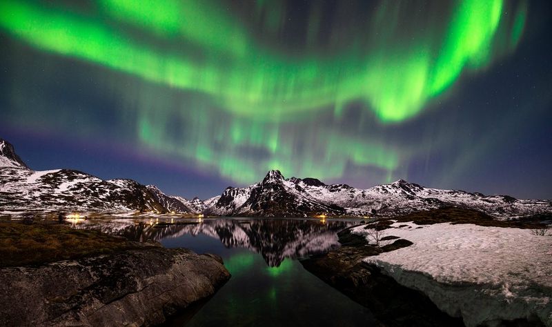 Questa foto di Harrison Brown mostra un'aurora boreale sopra un paesaggio innevato, le luci di un verde brillante si stagliano contro il cielo notturno.
