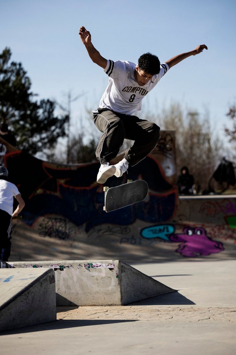 Een skateboarder in de lucht met uitgespreide armen en een draaiend board onder zich.