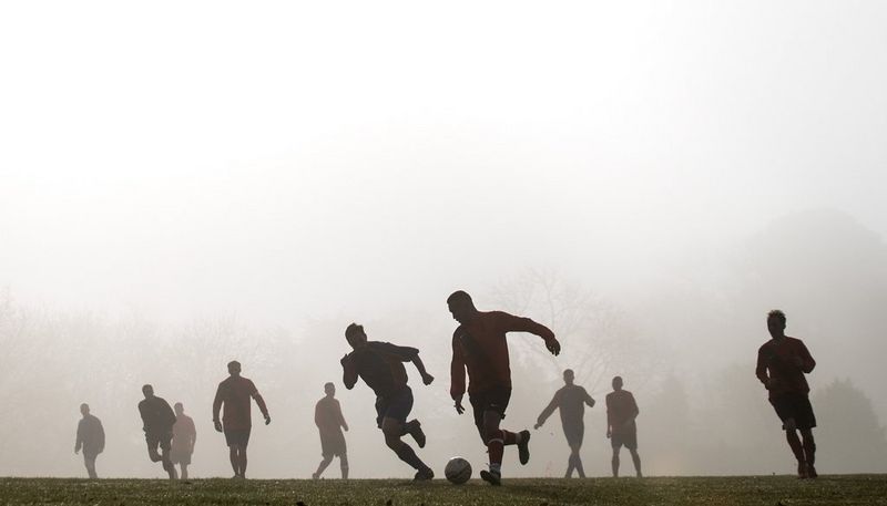 De silhouetten van de spelers worden zichtbaar als de zon doorbreekt in de vroege ochtendmist tijdens een voetbalwedstrijd.