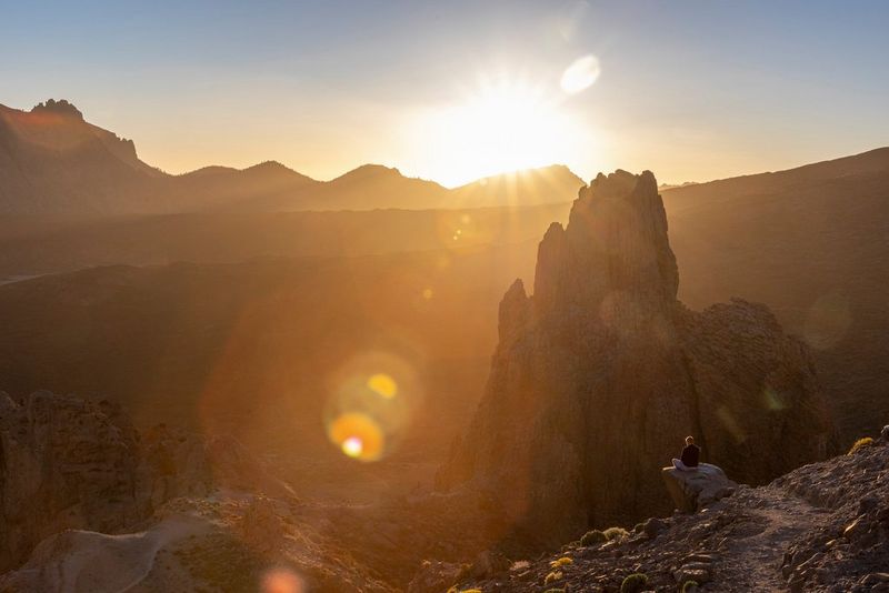 Солнце встает на фоне скалистого образования песчаного цвета.