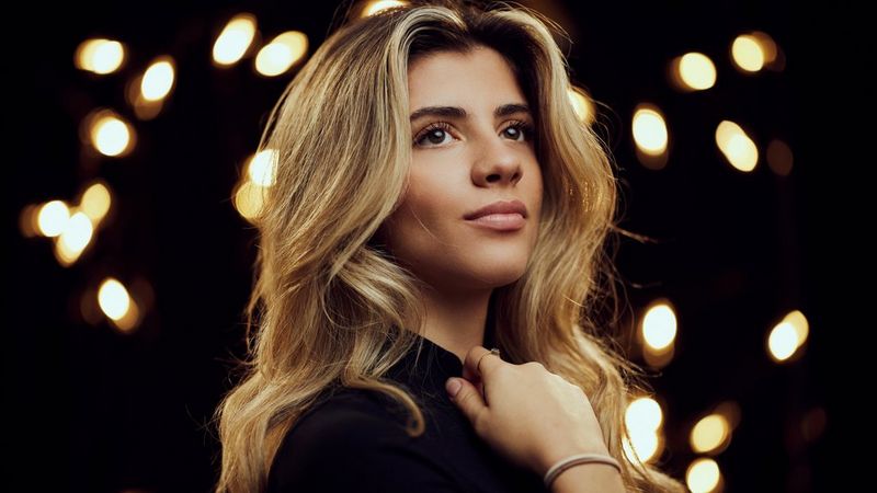 Ein Model, fotografiert vor einem dunklen Hintergrund mit unscharfen Lichtern, die das Bokeh betonen. Aufgenommen mit einem Canon RF 85mm F1.4 L VCM Objektiv.