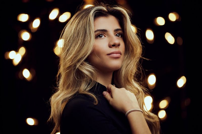A model photographed against a dark backdrop with blurred lights accentuating the bokeh. Taken using a Canon RF 85mm F1.4L VCM lens.