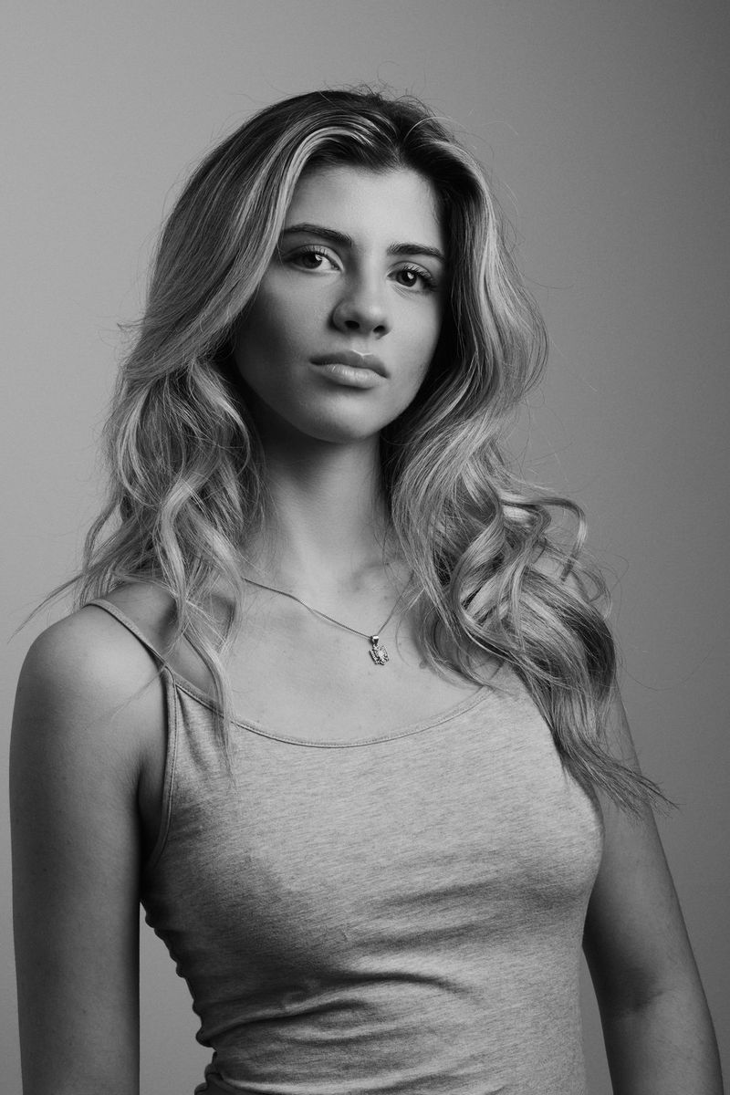 An informal monochrome portrait of a model standing in front of a plain-coloured backdrop, taken using a Canon RF 85mm F1.4L VCM hybrid lens.
