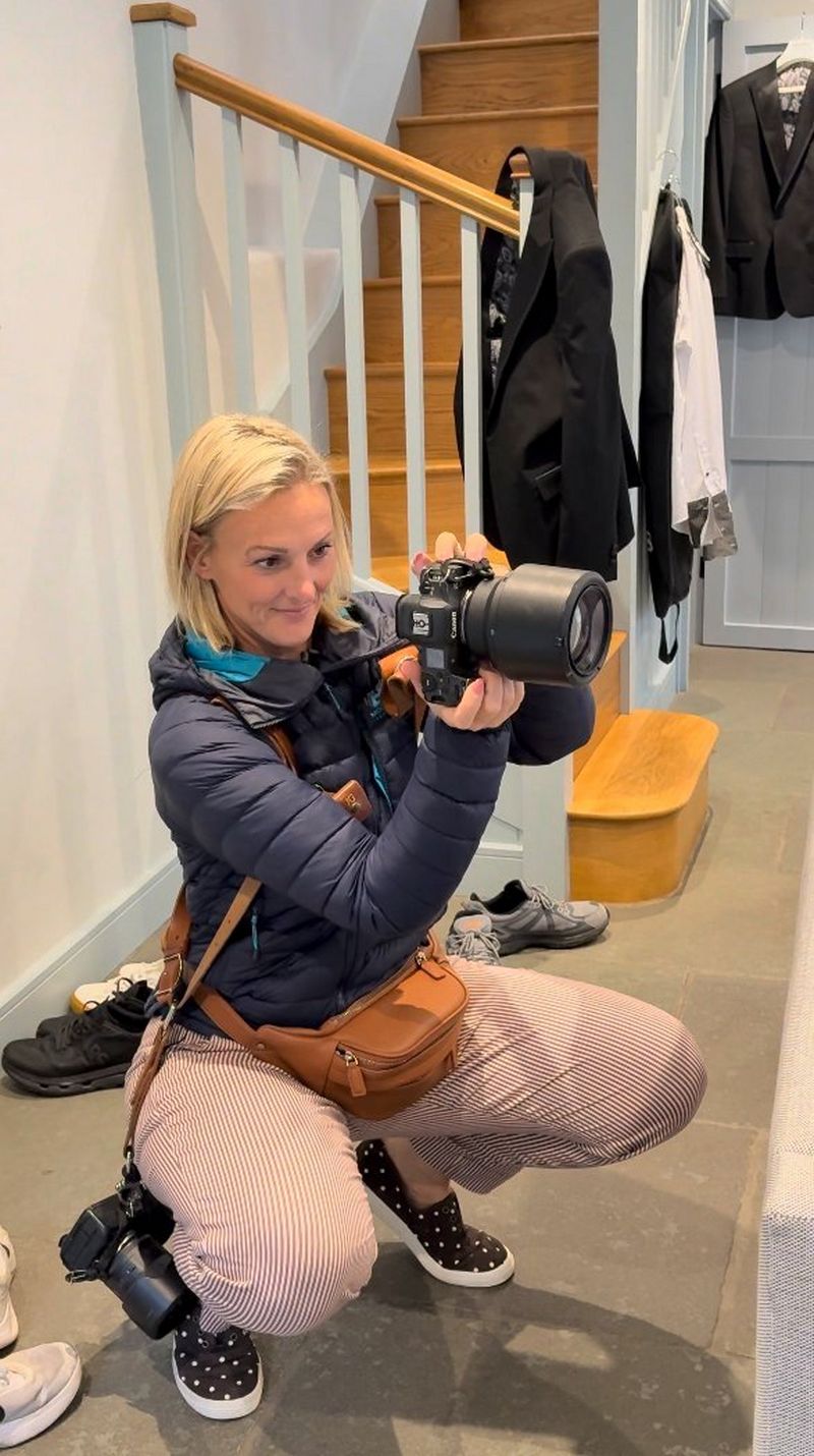 Wedding photographer and videographer Jo Greenfield at work, squatting to take a picture of the wedding prep, shooting with a Canon EOS R5 camera while another hangs at her side, ready for use.