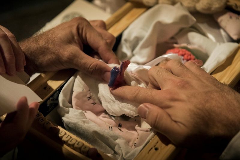 Мужчина и женщина держат ножку мертворожденного младенца, покрытую чернилами, чтобы создать ее отпечаток на листе бумаги.