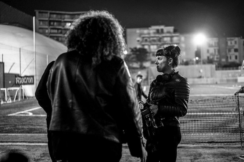 A monochrome photograph of Francesca Tosarelli holding a Canon EOS C70 at the Dorico Stadium in Ancona, Italy, while filming her women's football documentary.