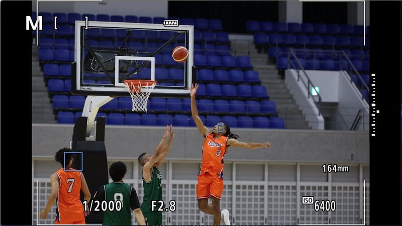 Баскетбольная игра через видоискатель камеры Canon EOS R1. Точка автофокусировки находится на игроке, который только что передал пас и собирается бежать к тому, кто получил пас и бросает мяч в кольцо.