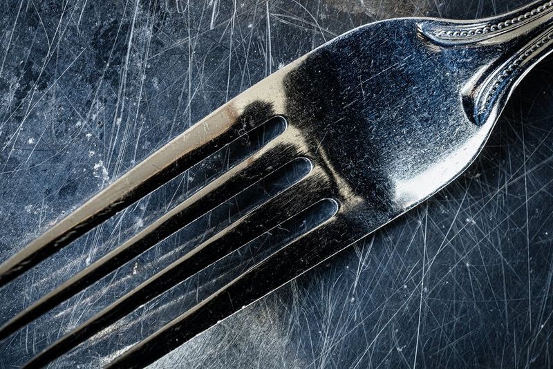 A closer view of a table fork on a dark, scratched work surface.
