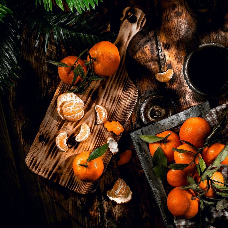 Mandarins arranged on a chopping board and tray on a dark wood table, one peeled with its segments spread out.