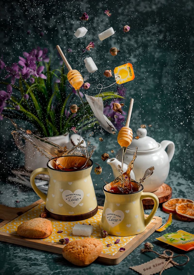 Sugar cubes, honey dippers and teabags suspended above two mugs of tea; splashes of liquid are frozen in motion above the rims of the mugs.