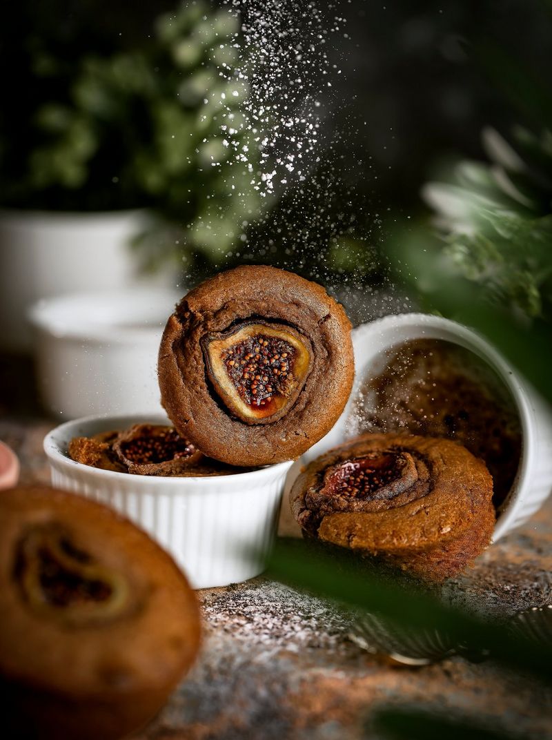 A dusting of icing sugar suspended in the air above pomegranate desserts baked in ramekins.