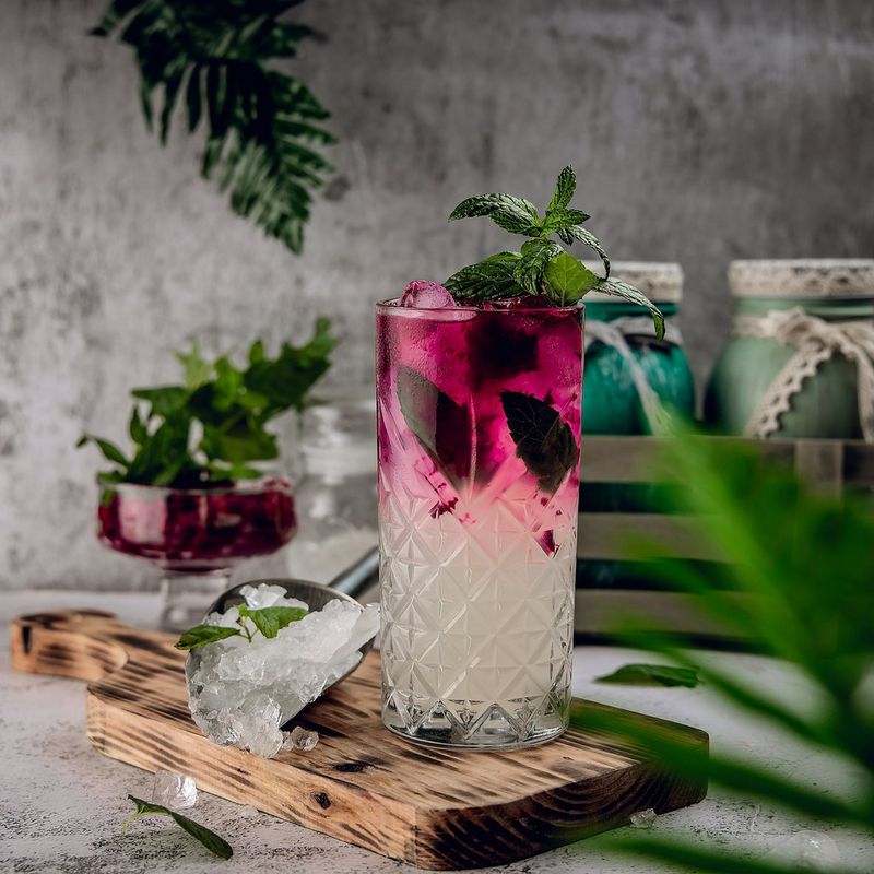 A tall glass filled with a colourful iced drink and garnished with mint.