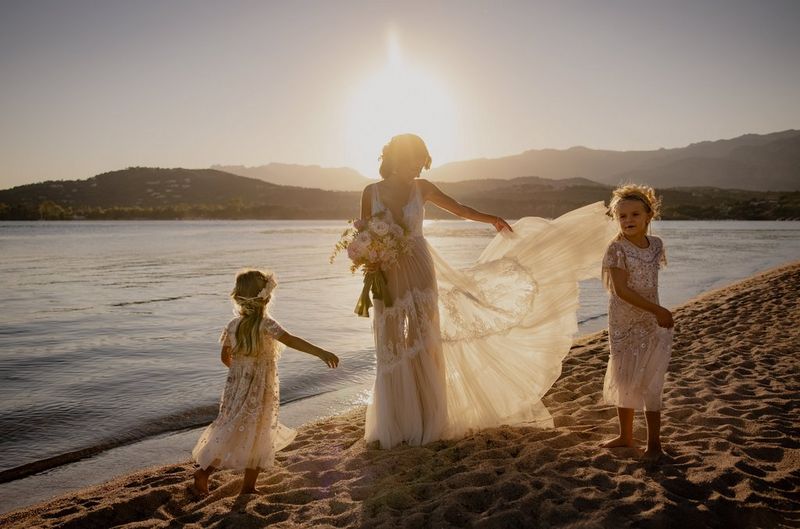 Una sposa e le sue due giovani damigelle fanno volteggiare i loro vestiti al tramonto su una spiaggia deserta.