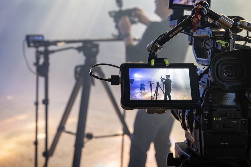 An external monitor showing footage of a man filming a music video on a Canon XA45 camcorder.