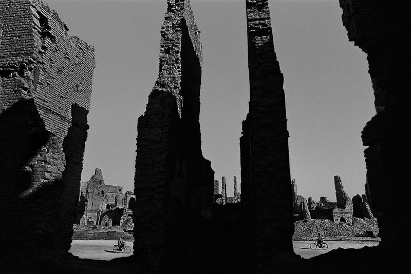 In this photograph captured by James Nachtwey in Kabul, Afghanistan in 1996, two people on bicycles can be seen on either side of the damaged pillars of a building.