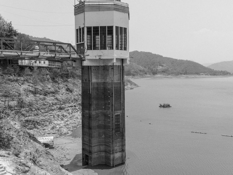 Черно-белое фото, созданное Жеромом Сессини на камеру Canon EOS R5, демонстрирует водонапорную станцию в системе водоснабжения Куцамала, Мексика, где уровень воды настолько низкий, что водонапорная башня видна практически целиком.