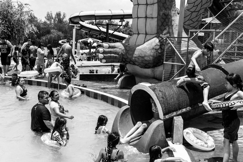 Черно-белое фото, созданное Жеромом Сессини на камеру Canon EOS R5, демонстрирует оживленный аквапарк в Мексике, где взрослые и дети радуются водным аттракционам.