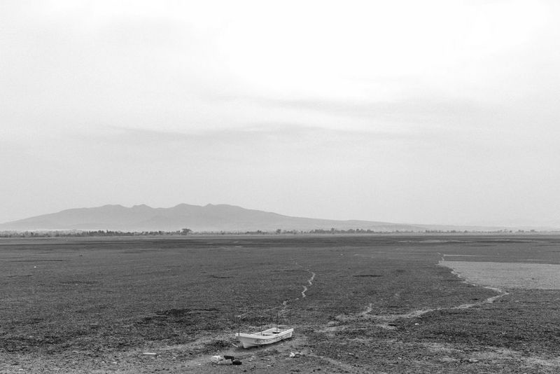 Черно-белое фото, созданное Жеромом Сессини на камеру Canon EOS R5, демонстрирует одинокую лодку, частично затонувшую в грязной бессточной области в озере Зумпанго.