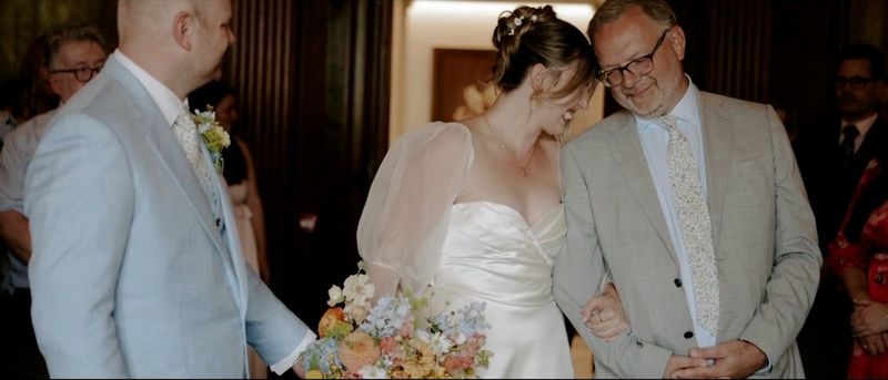 A bride and her father share a smile as they approach the groom. Still from a video taken on a Canon EOS R5 by wedding photographer and videographer Jo Greenfield.
