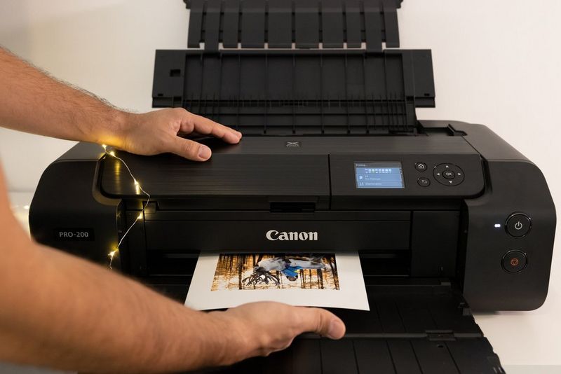 A hand holds the underside of an A4 print as its emerges from a Canon printer.