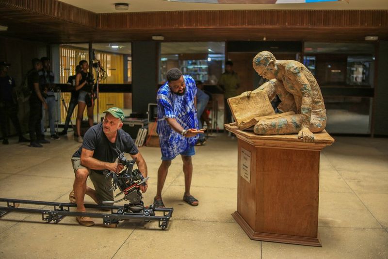 Kunle Afolayan and DoP Jonathan Kovel set up a shot in front of a statue of a man reading, with a Canon EOS C500 Mark II camera mounted on a slider.