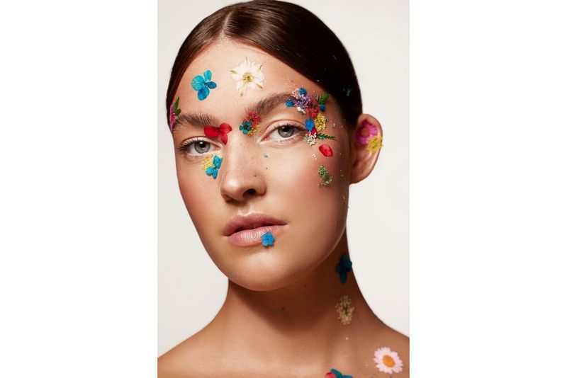 A beauty portrait of a model with colourful flowers applied to her skin, taken with a Canon RF 100mm F2.8L MACRO IS USM lens.