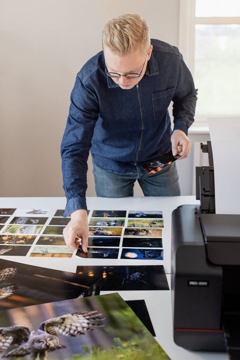 A man leans over a table, laying out small prints of nature photographs in a grid.