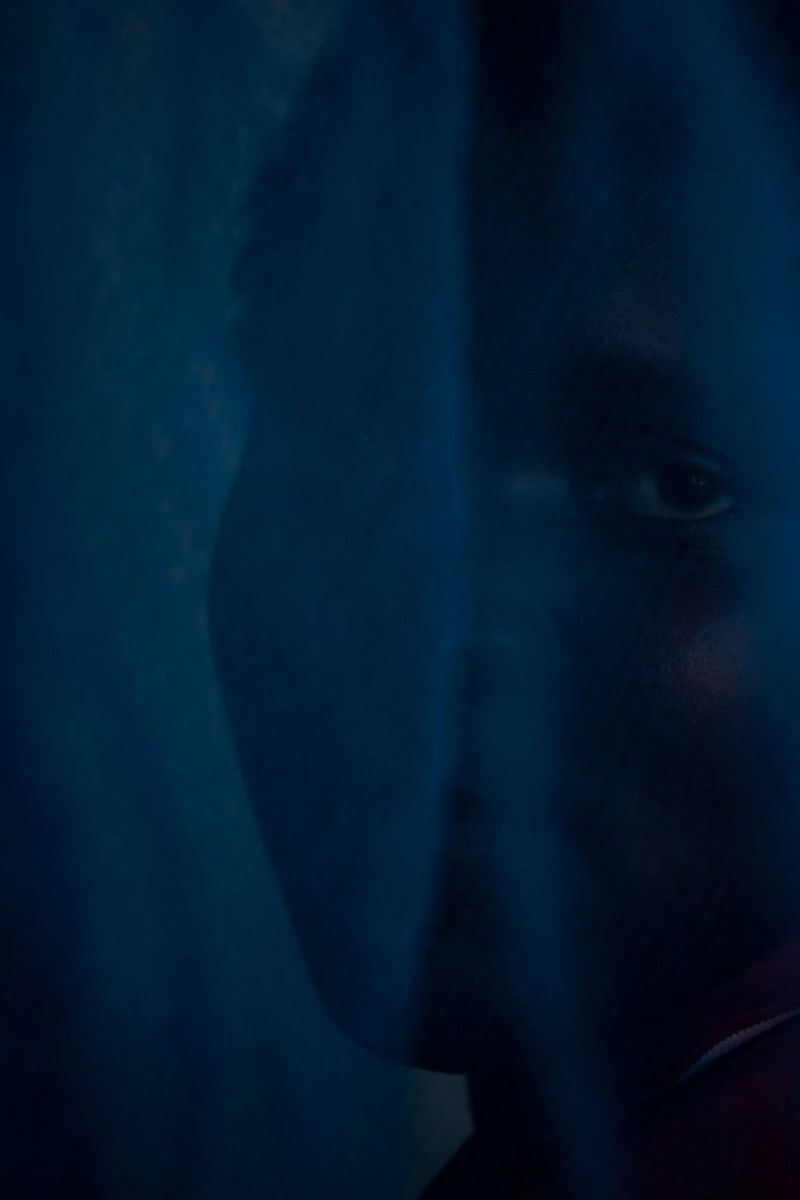  A woman peaks through a blue hospital curtain, captured on a Canon EOS R5 by Laura El-Tantawy for her series Carrying Life: Motherhood and Water in Malawi.